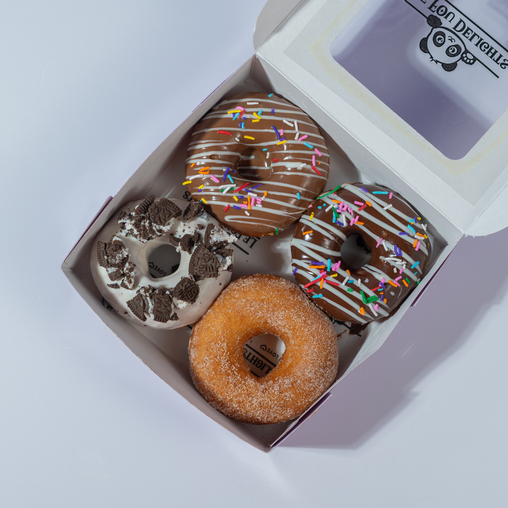 Pack of 4 donuts in Vadodara by Le Fou Delights with chocolate drizzle, colourful sprinkles, cookie topping, and sugar-coated donut.