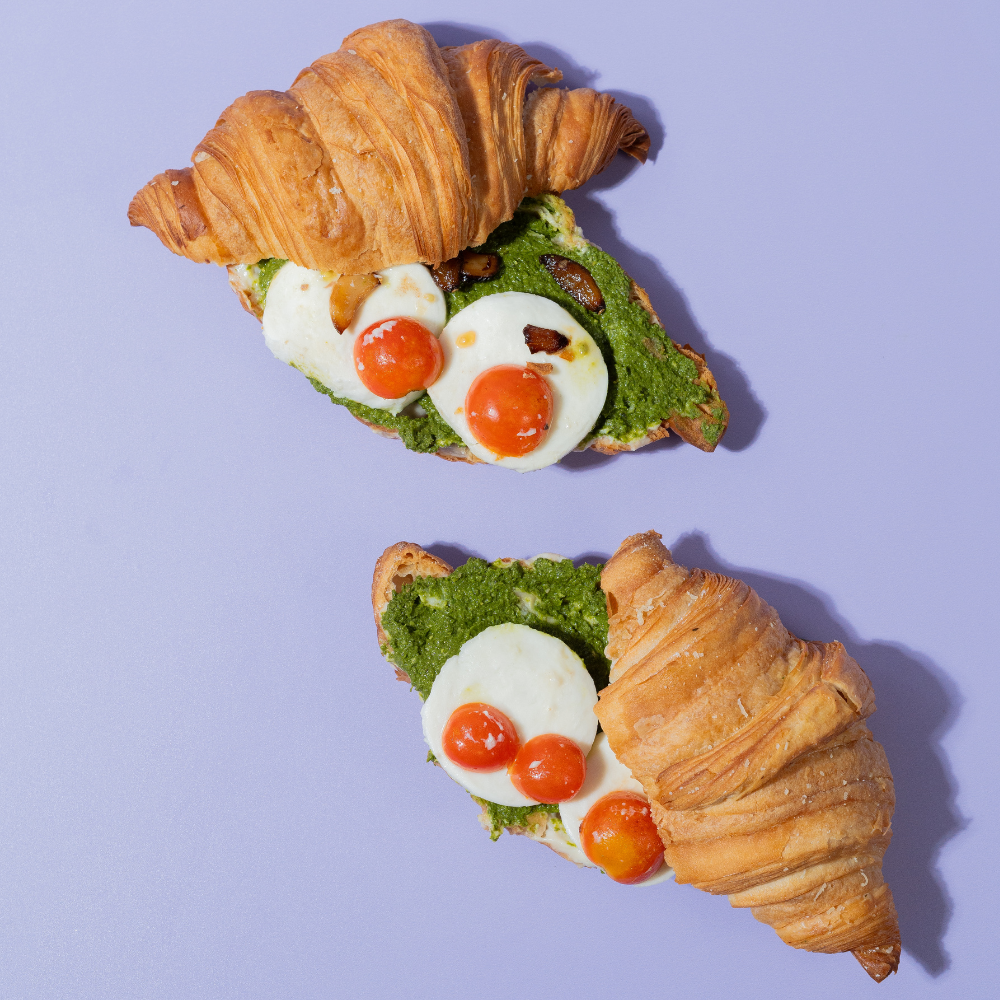 Savory Caprese croissant sliced open to show melted mozzarella cheese, fresh tomato, and green pesto filling