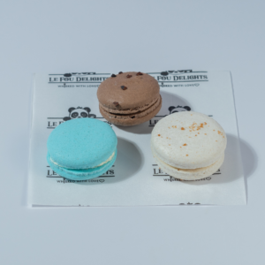 Pack of 3 macarons in Vadodara by Le Fou Delights featuring chocolate, blue, and white macarons with creamy fillings.
